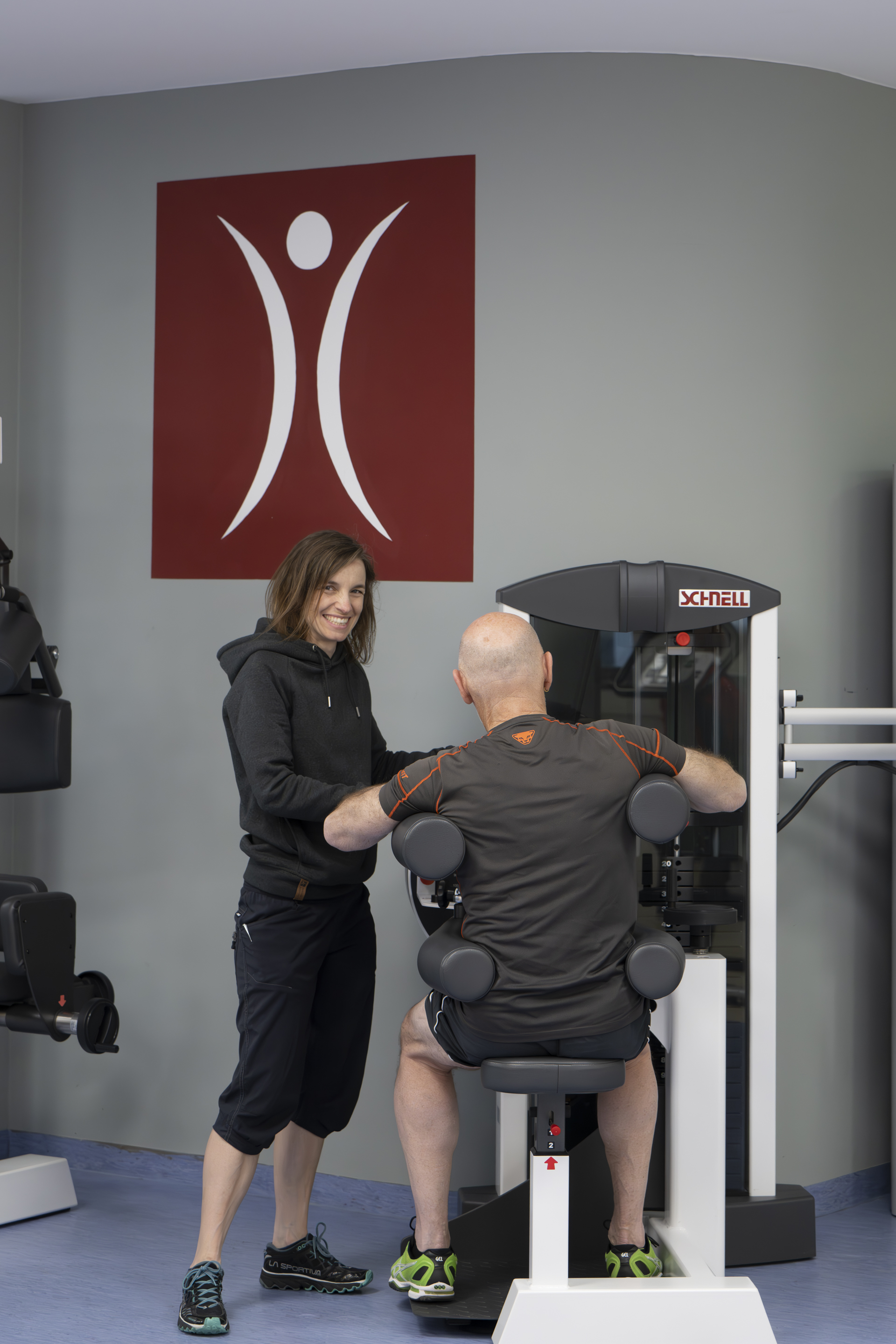Patient wir von Sporttherapeutin an einem Rücken-Fitness-Gerät angeleitet.